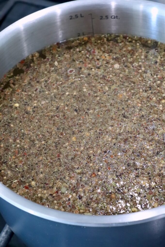 A silver pot filled with a simmering mixture of seeds and spices in liquid