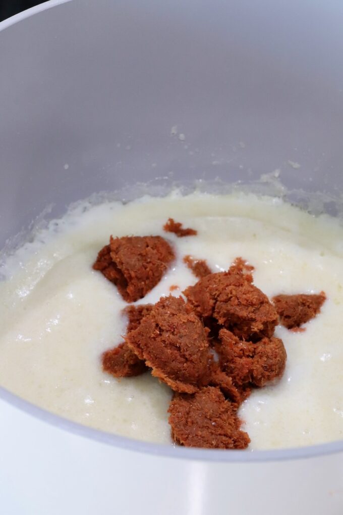 creamy roux sauce in a pot topped with spoonfuls of red curry paste