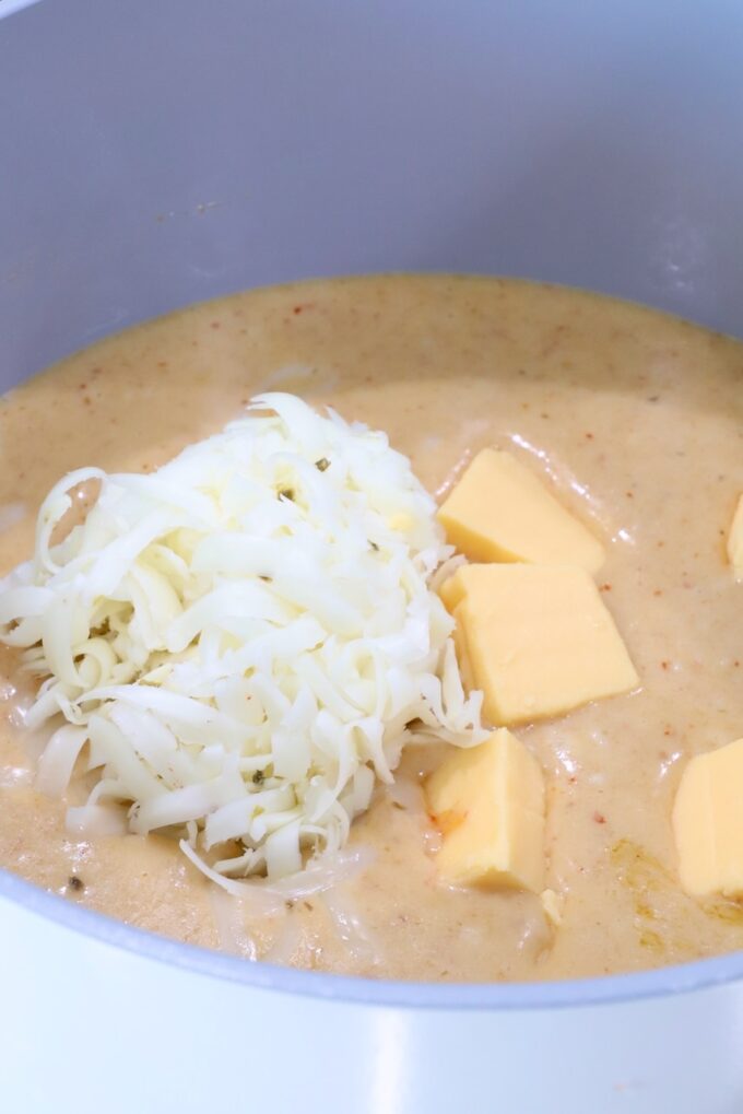 creamy red curry sauce in a pot with cubed Velveeta cheese and shredded pepper jack cheese