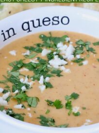 A creamy curry queso dip in a white bowl garnished with chopped cilantro and crumbled cheese