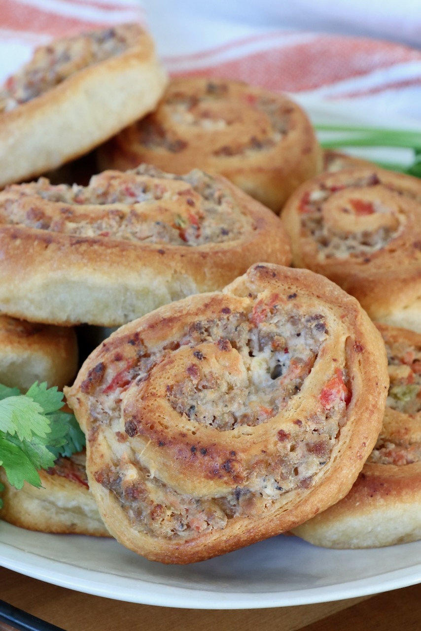 Close-up of savory swirled pastry rolls with a golden, crispy crust. Filled with sausage and tomatoes, garnished with fresh cilantro, on a white plate.