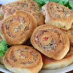 Close-up of savory swirled pastry rolls with a golden, crispy crust. Filled with sausage and tomatoes, garnished with fresh cilantro, on a white plate.