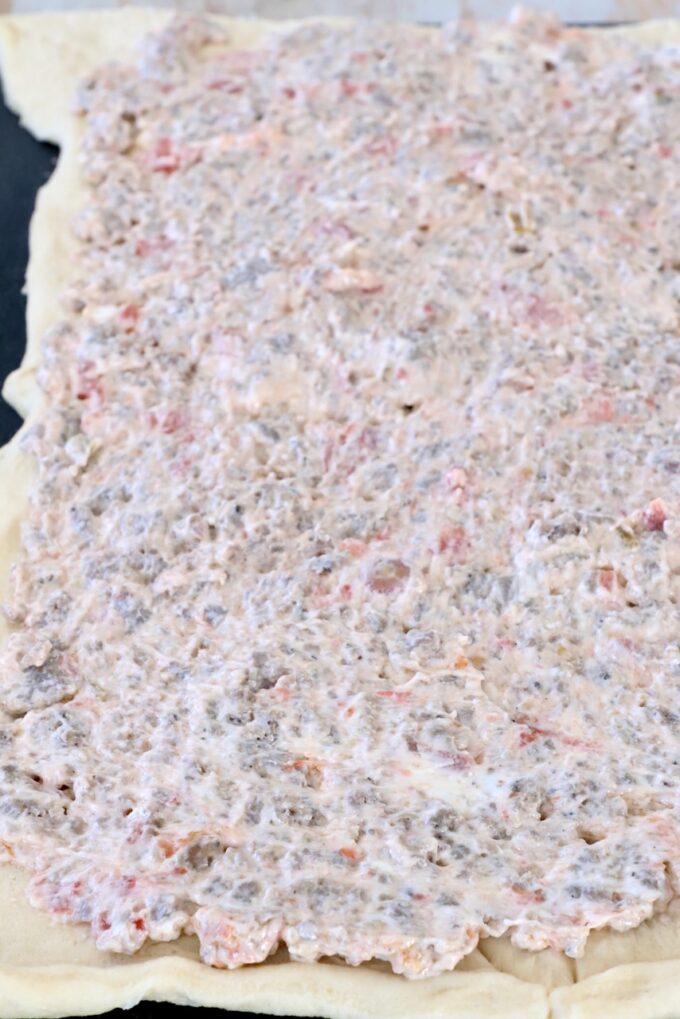 crescent roll dough covered in a cream cheese sausage mixture on a cutting board