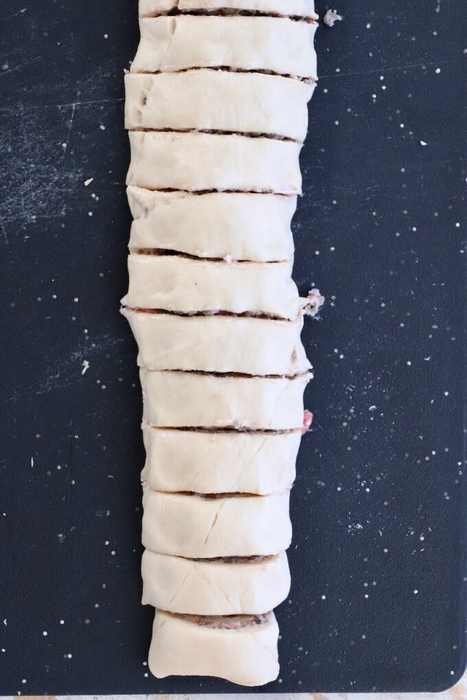 Dough rolled up with filling, sliced into even pieces, laid vertically on a black surface