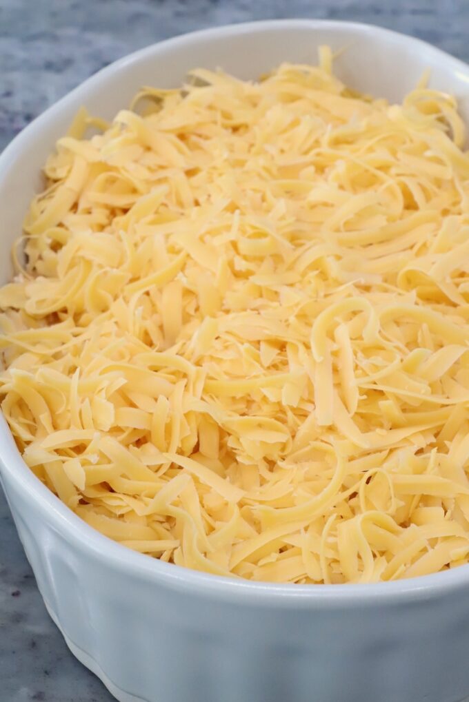 A white ceramic dish filled with freshly grated cheddar cheese on top of hot honey chicken dip