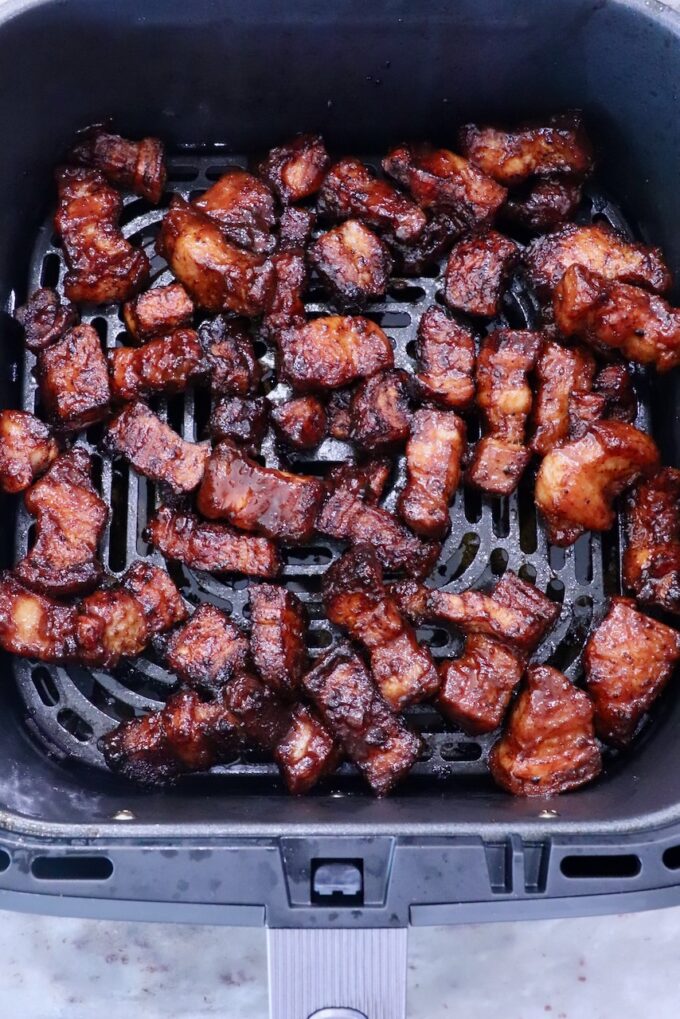 Crispy, golden-brown pork belly pieces in an air fryer basket, showing a rich glaze and succulent texture.