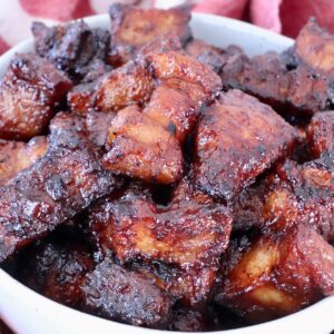 Close-up of glazed, caramelized pork belly bites in a white bowl
