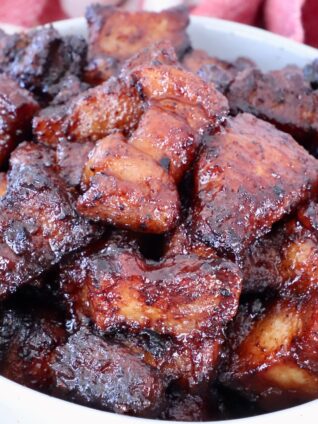 Close-up of glazed, caramelized pork belly bites in a white bowl