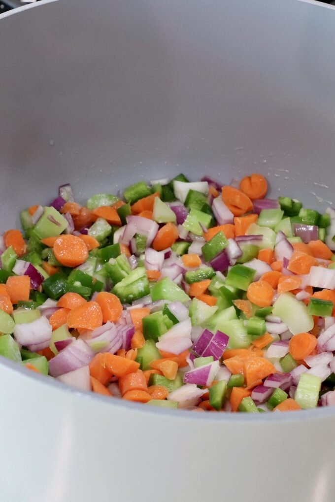 Chopped vegetables, including carrots, green peppers, onions, and celery, in a large gray pot
