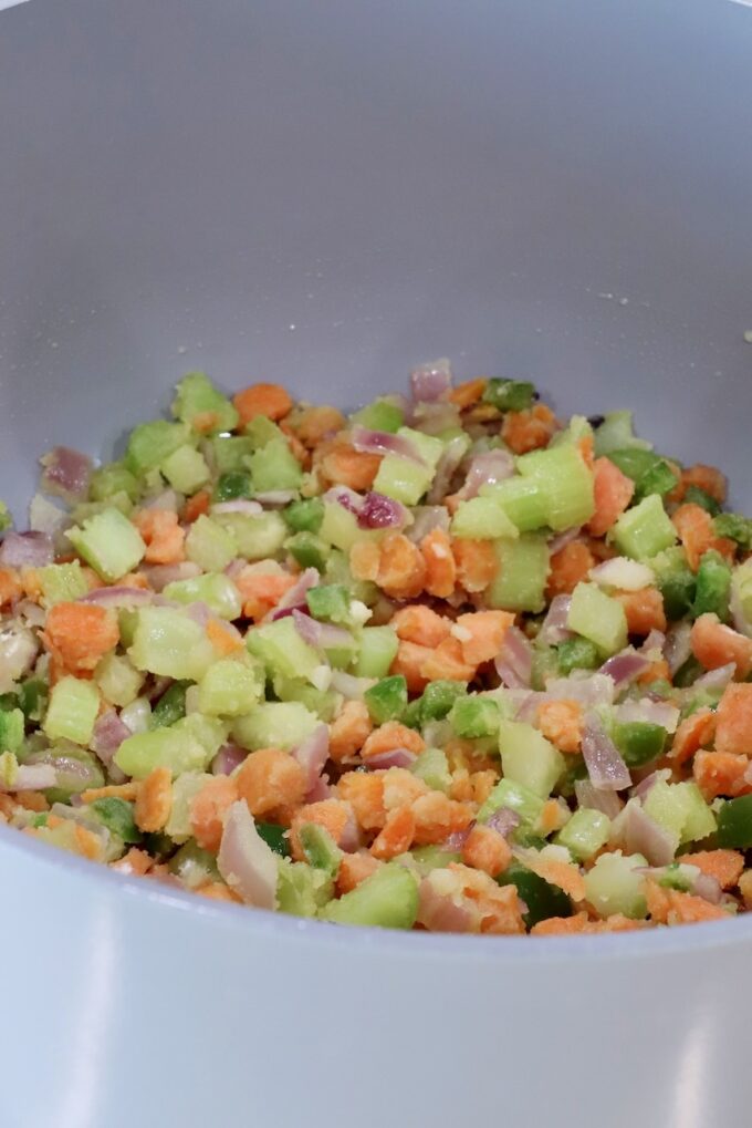Chopped vegetables, including carrots, jalapeno peppers, onions, and celery, in a large gray pot, covered in flour