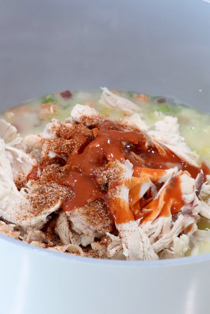 shredded chicken covered in seasonings and buffalo sauce in a pot with vegetables