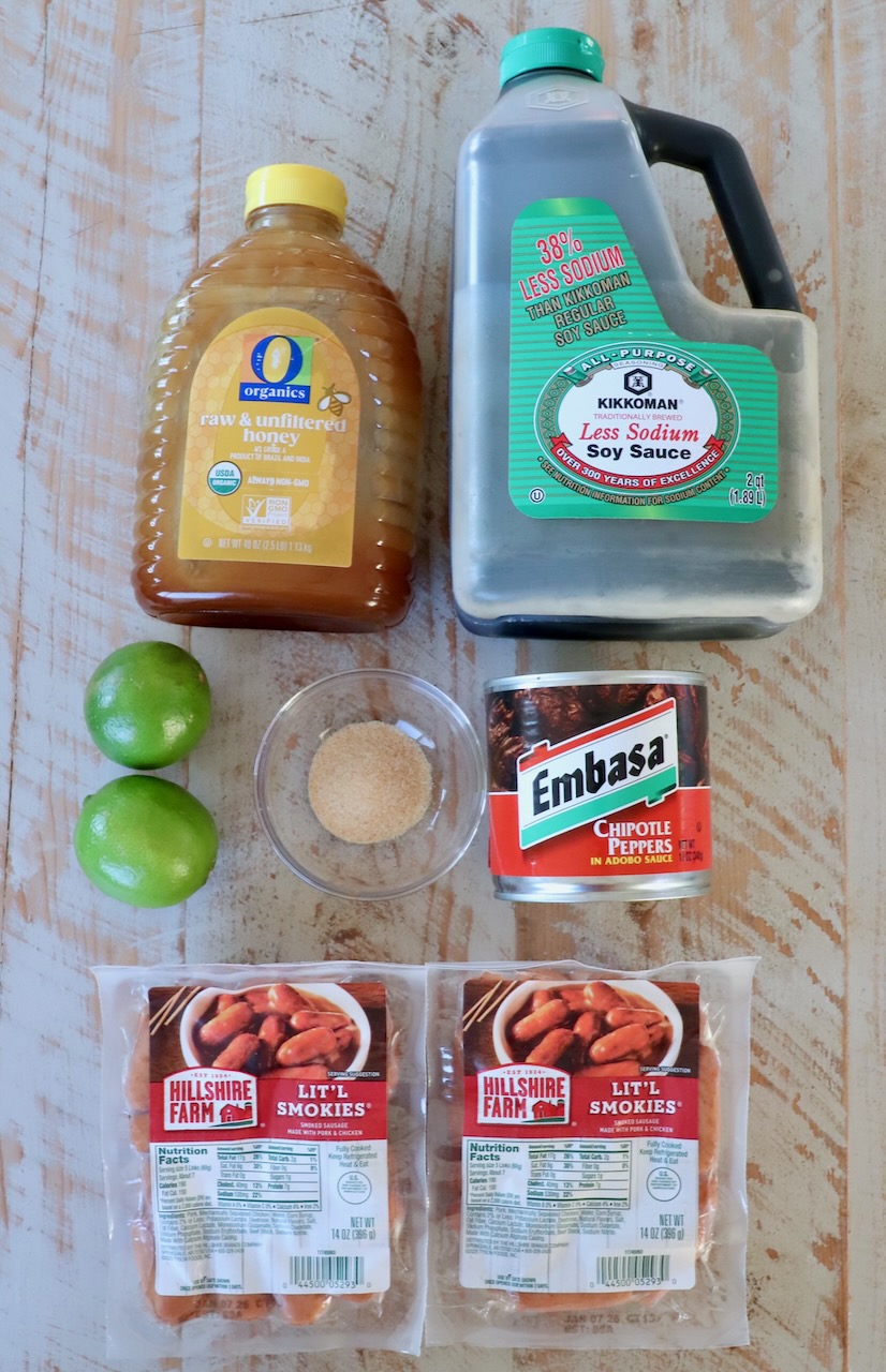 Assorted ingredients on a wooden surface include honey, low-sodium soy sauce, chipotle peppers, brown sugar, limes, and two packs of Lit'l Smokies sausages.