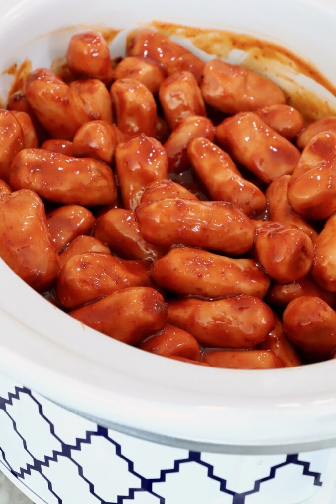 A white crockpot filled with small sausages in a rich, glossy chipotle honey sauce.