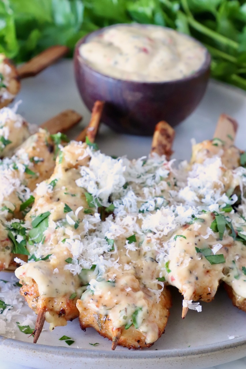 air fried chicken skewers topped with creamy sauce, garnished with fresh herbs and grated cheese. A small bowl of dipping sauce is in the background.
