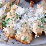cooked chicken skewers drizzled with a creamy sauce, topped with shredded cheese and fresh herbs, on a light-colored plate.