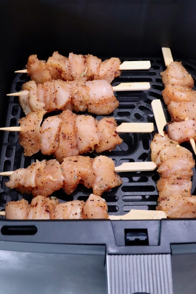 Raw chicken skewers seasoned with spices are arranged in an air fryer basket, ready for cooking.