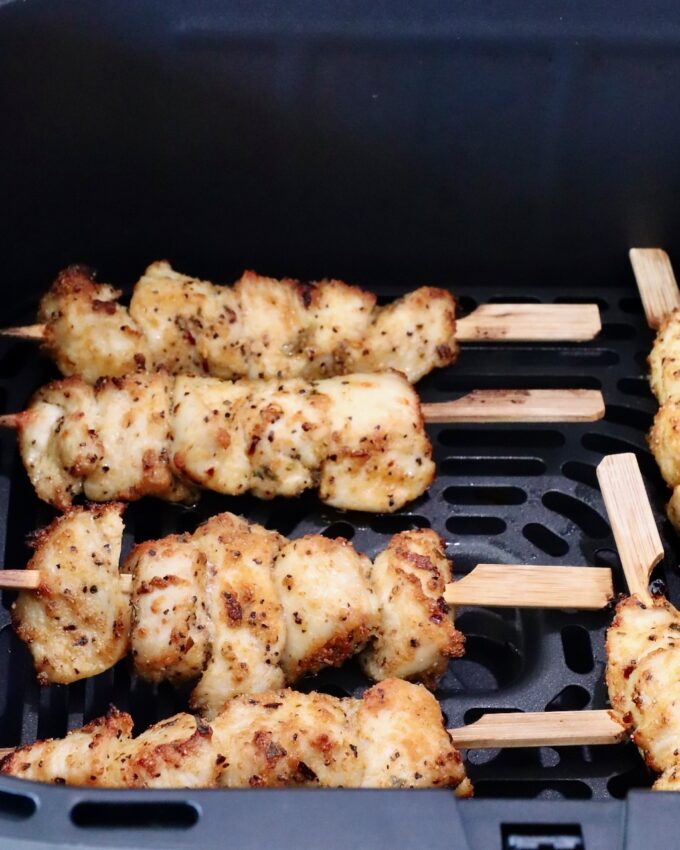 Cooked golden brown chicken skewers seasoned with herbs placed in an air fryer basket.