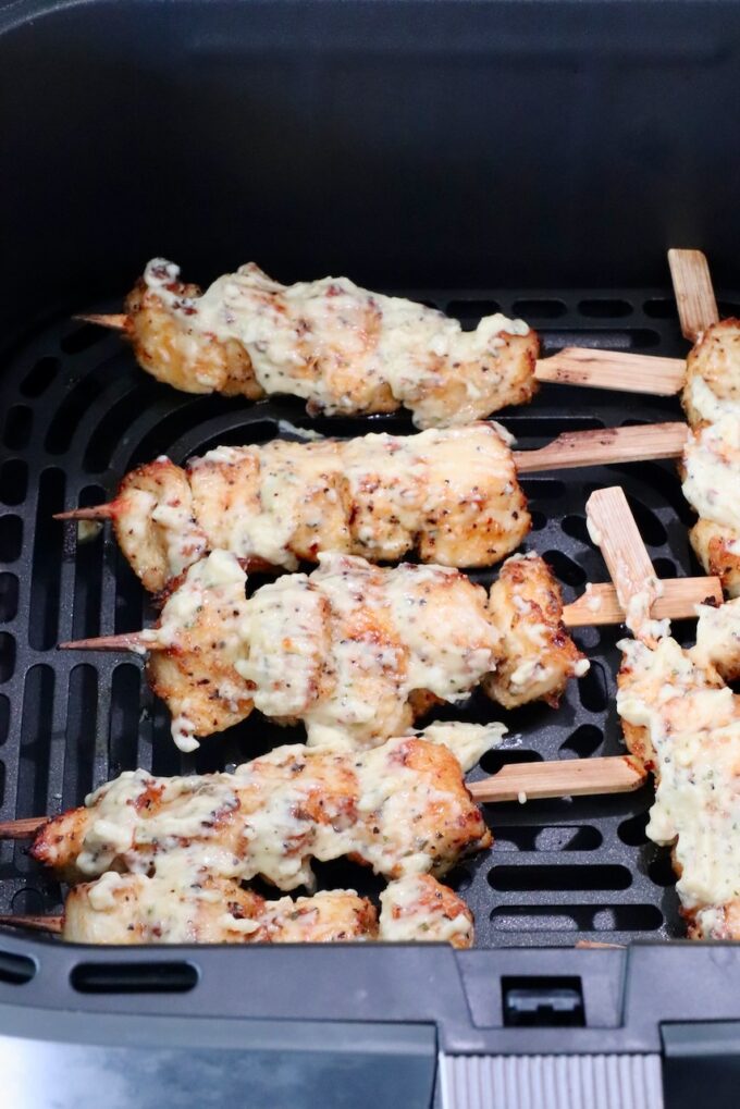 Cooked chicken skewers topped with creamy sauce in an air fryer basket.