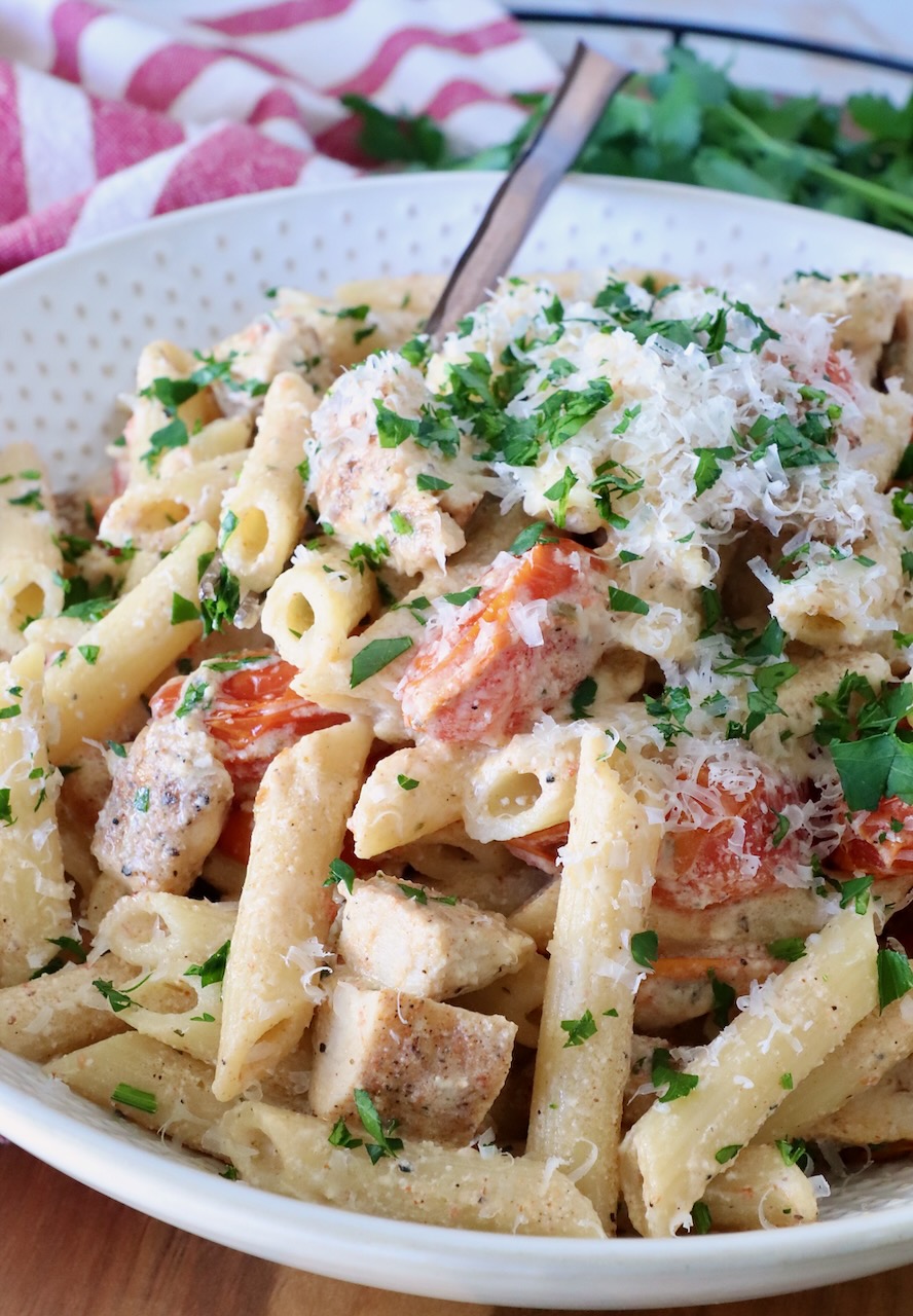A creamy pasta dish with penne, diced chicken, cherry tomatoes, and parsley, topped with grated cheese.
