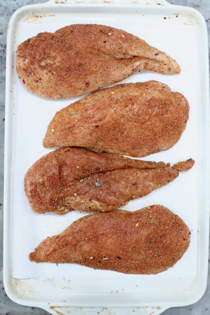 seasoned raw chicken breasts on a white baking sheet