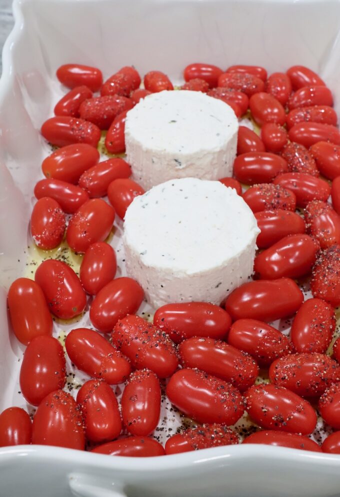 two rounds of Boursin cheese in a baking dish surrounded by cherry tomatoes