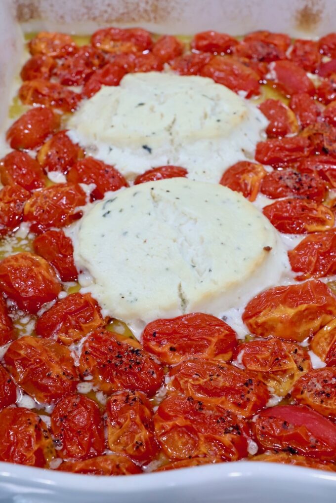 two rounds of melted Boursin cheese in a baking dish surrounded by roasted cherry tomatoes