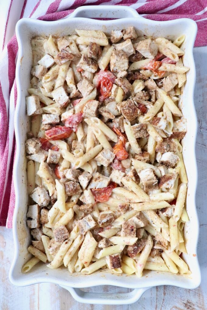 penne pasta in a creamy sauce with roasted tomatoes and diced chicken in a baking dish