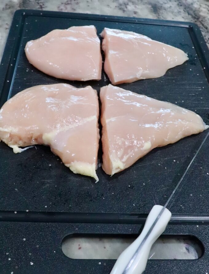 chicken breasts cut in half on a cutting board, sitting next to a knife
