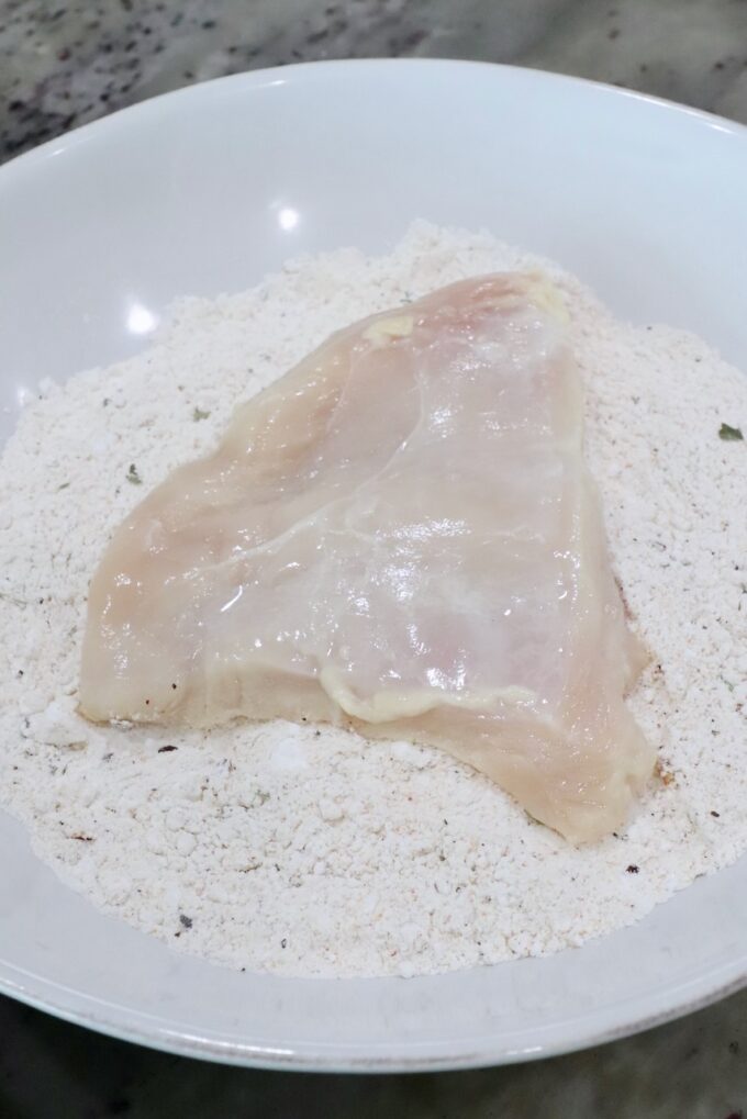 piece of chicken in a bowl of seasoned flour