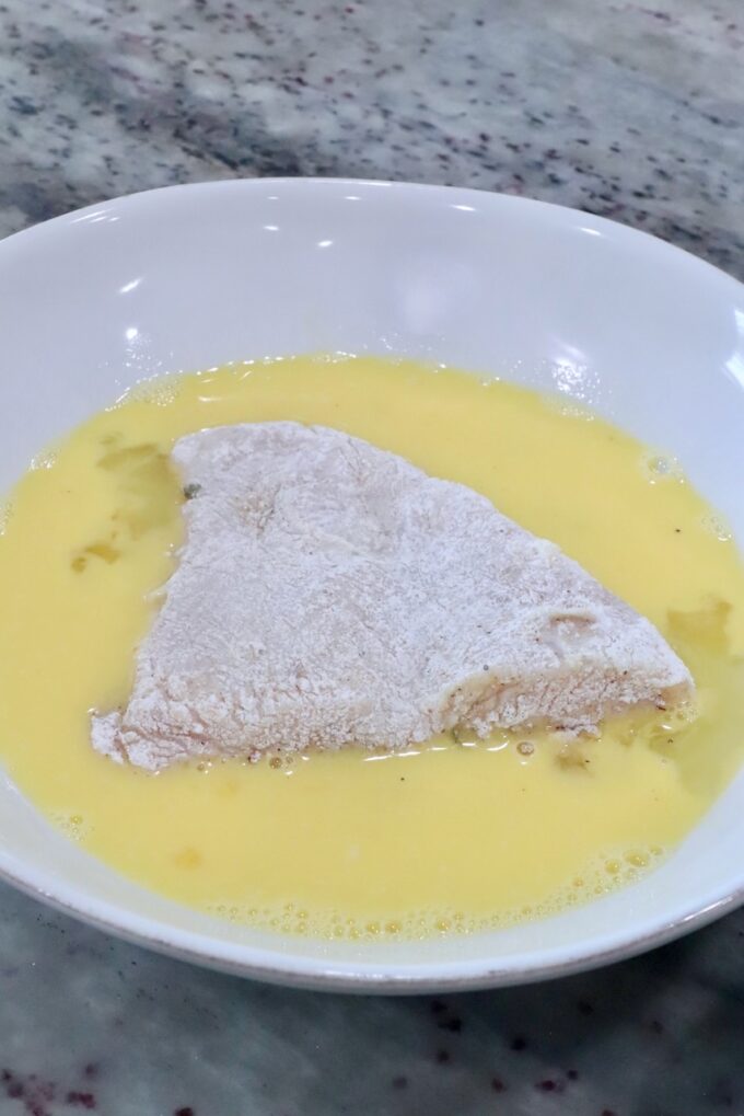 flour-coated chicken in a bowl of whisked eggs