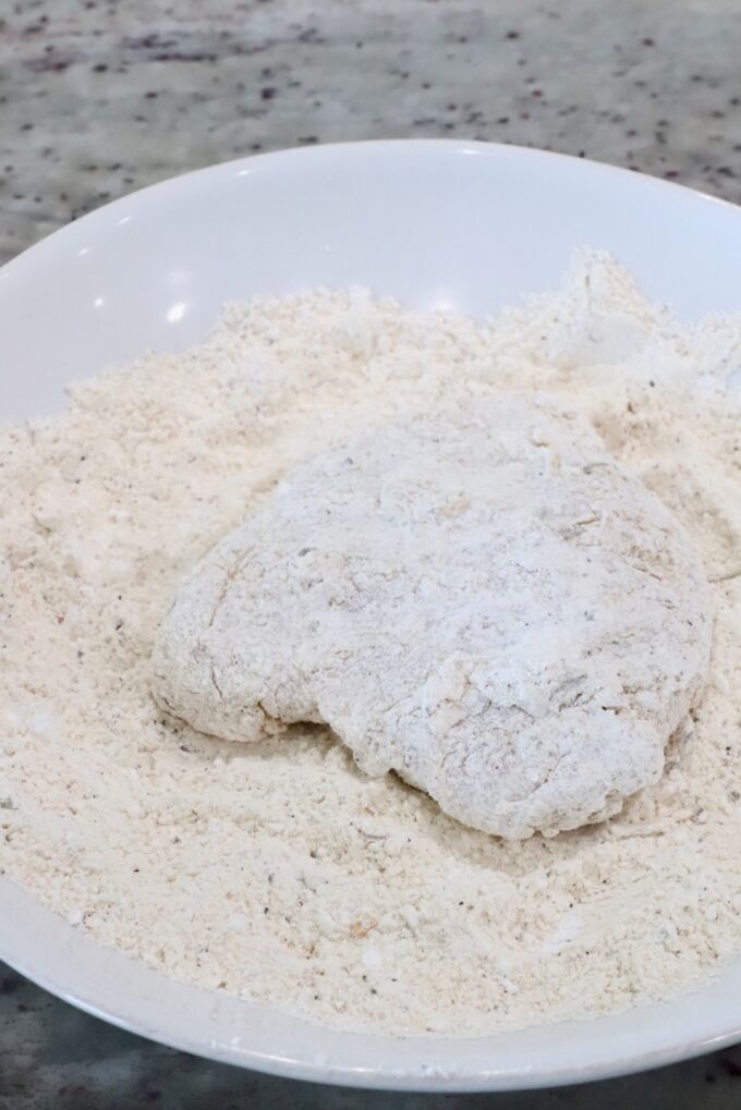 a piece of coated chicken in a bowl of flour