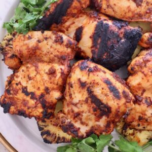 Grilled chicken thighs with charred marks on a white plate, garnished with fresh cilantro.