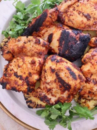Grilled chicken thighs with charred marks on a white plate, garnished with fresh cilantro.