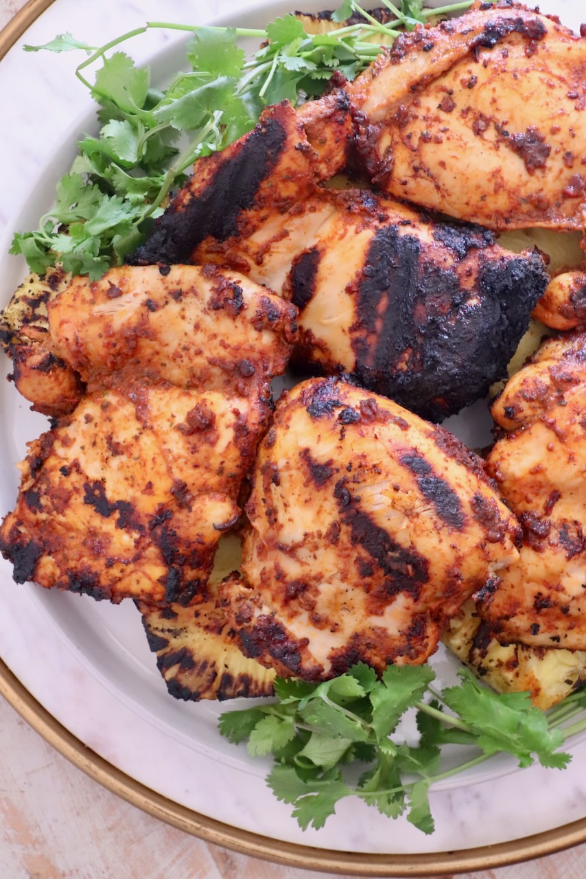 Grilled chicken thighs with charred marks on a white plate, garnished with fresh cilantro.