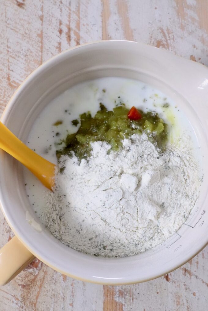 Mixing bowl with ranch dressing mix, buttermilk, and dill pickle relish. A yellow spatula rests in the bowl on a wooden surface.