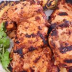 Grilled chicken thighs with charred marks on a white plate, garnished with fresh cilantro.