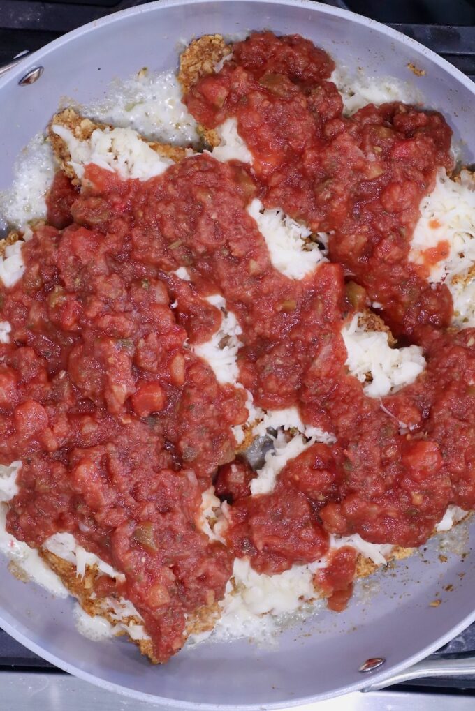 Pan-fried breaded chicken breasts topped with melted cheese and chunky salsa in a skillet.