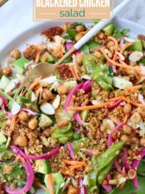 Fresh salad with crispy quinoa, blackened chicken, chickpeas, carrots, almonds, and greens on a plate with a fork.