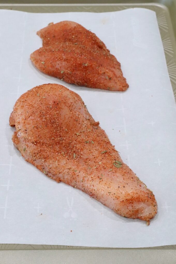 seasoned chicken breasts on a parchment-lined baking sheet