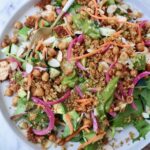 A vibrant salad with greens, quinoa, chickpeas, sliced almonds, carrots, and pickled onions on a plate with a fork.