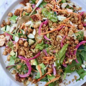 A vibrant salad with greens, quinoa, chickpeas, sliced almonds, carrots, and pickled onions on a plate with a fork.