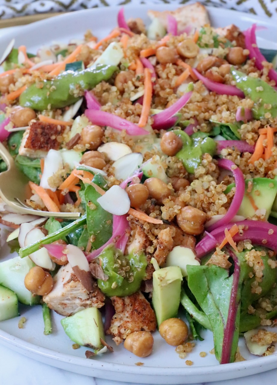 A vibrant salad with greens, quinoa, chickpeas, sliced almonds, carrots, and pickled onions on a plate.