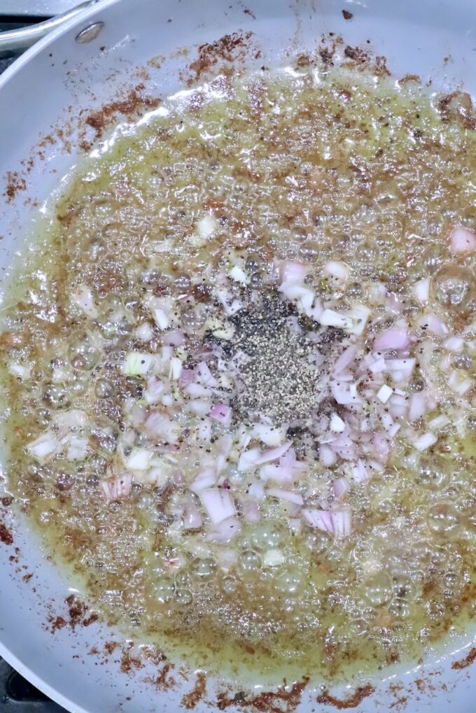 shallots and black pepper in liquid in a skillet