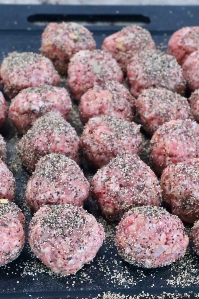 raw meatballs covered in black pepper on a dark cutting board