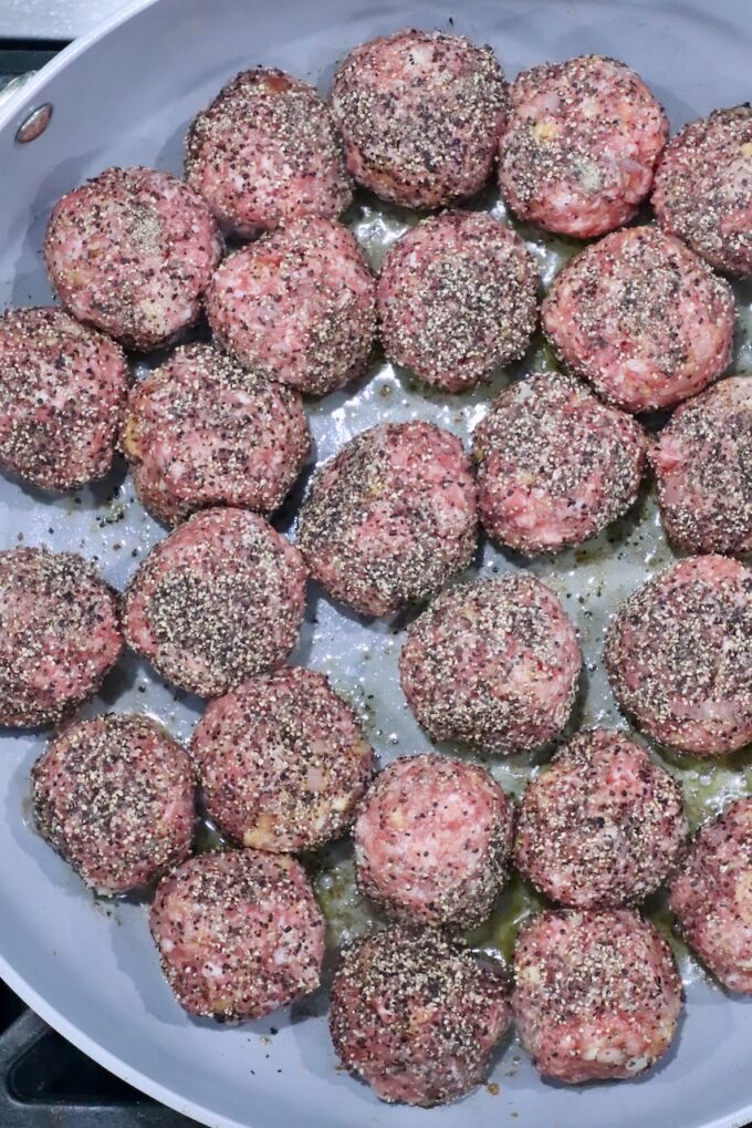 pepper coated raw meatballs in a skillet