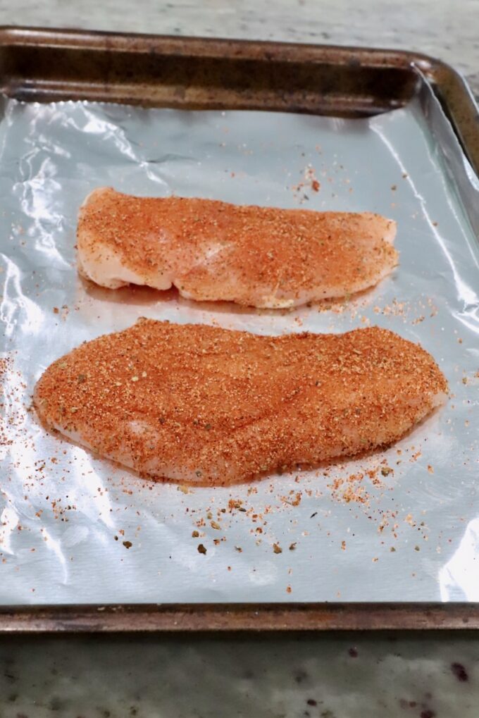 seasoned raw chicken breasts on a foil-lined baking sheet