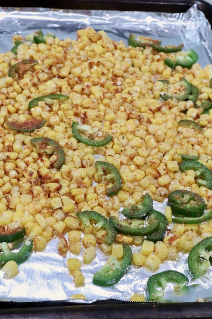 seasoned corn kernels and sliced jalapenos on a foil-lined baking sheet