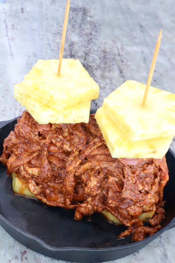 thinly sliced marinated pork stacked up on skewers with pineapple slices in a cast iron skillet